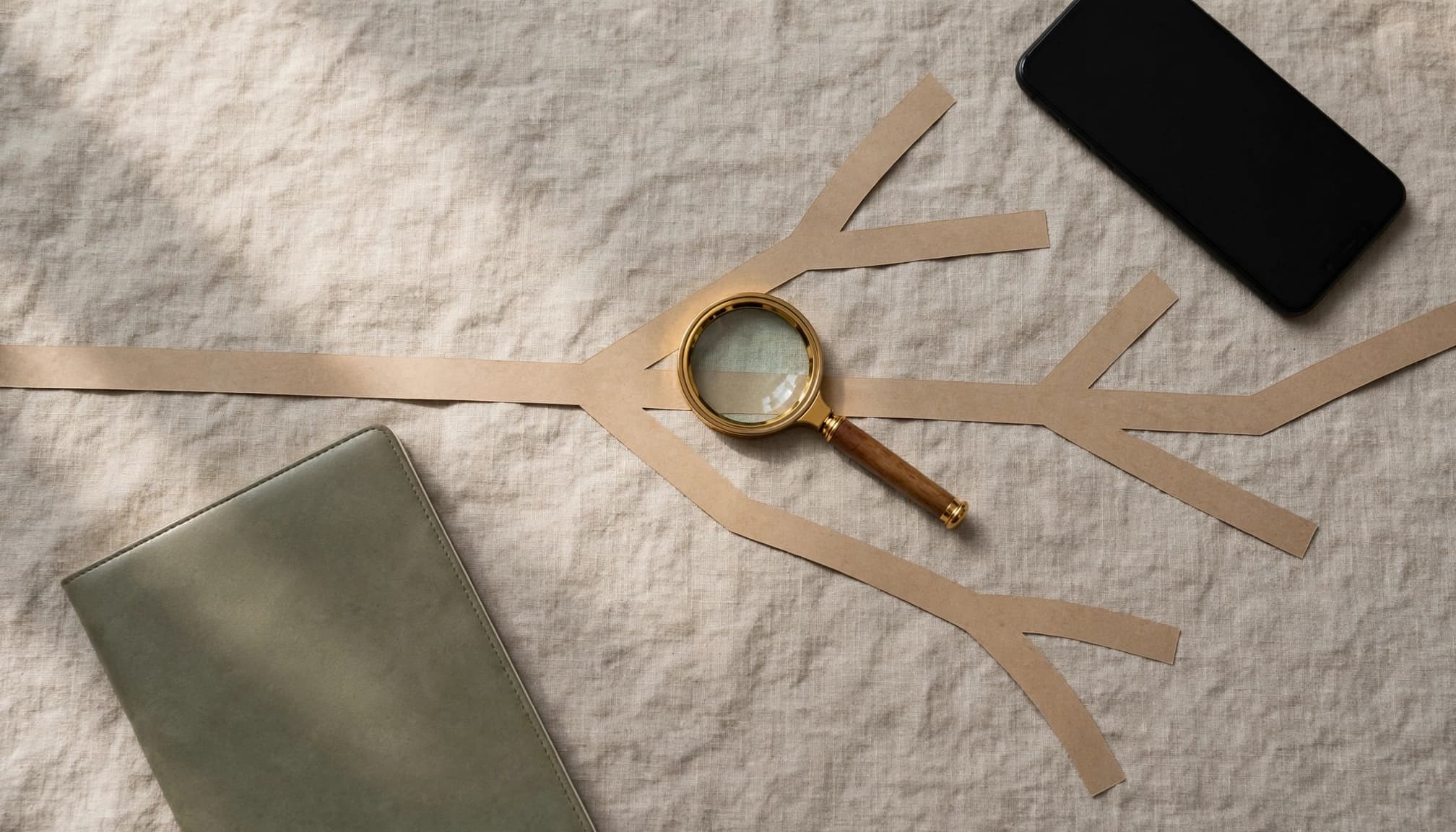 A notebook, face-down phone, branching paper path, and small magnifying glass.