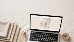 A laptop, skincare bottle, fabric swatches, and measuring tape arranged on a bright desk.