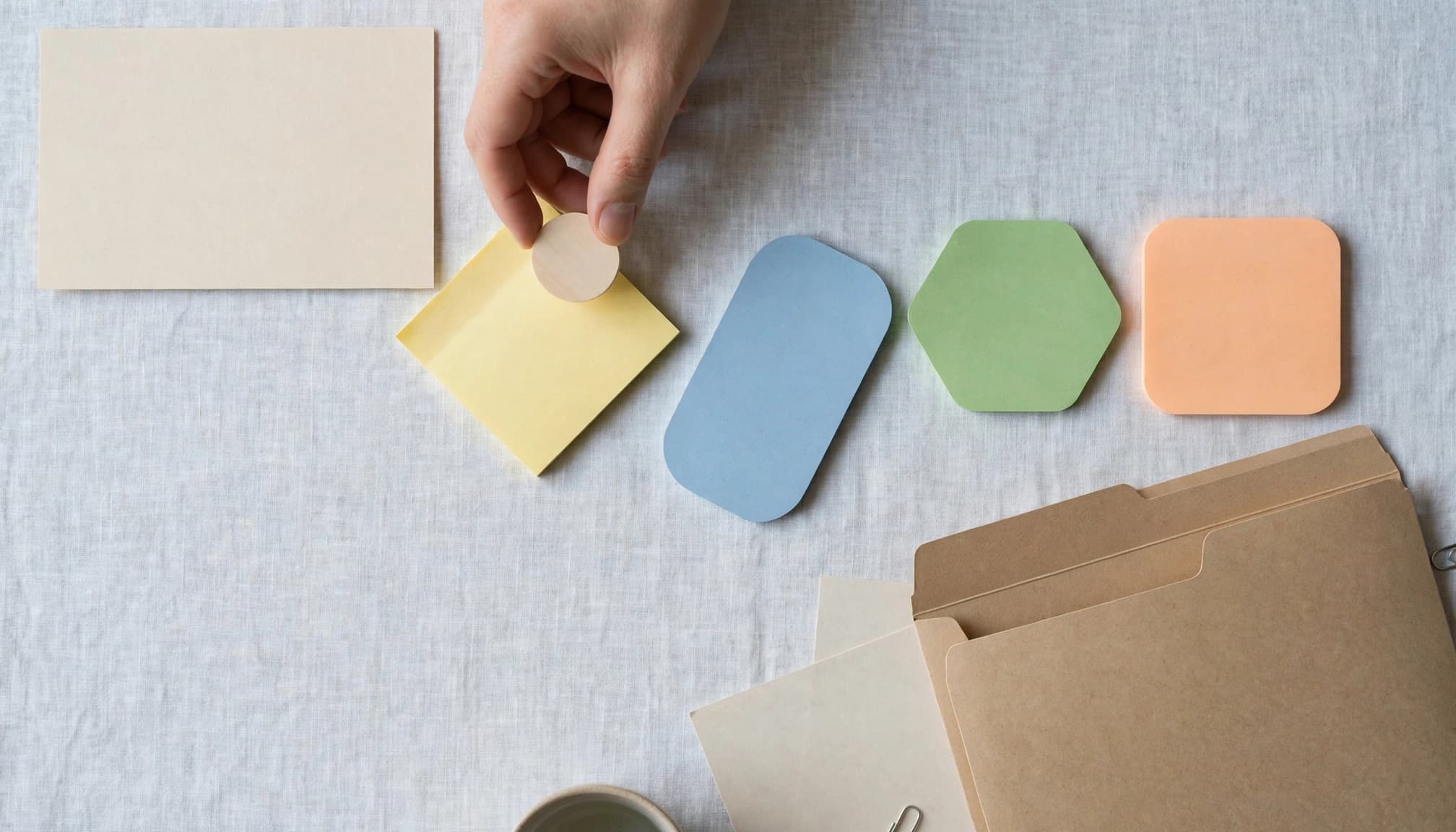 A hand places a blank token beside colored paper shapes leading toward a folder.