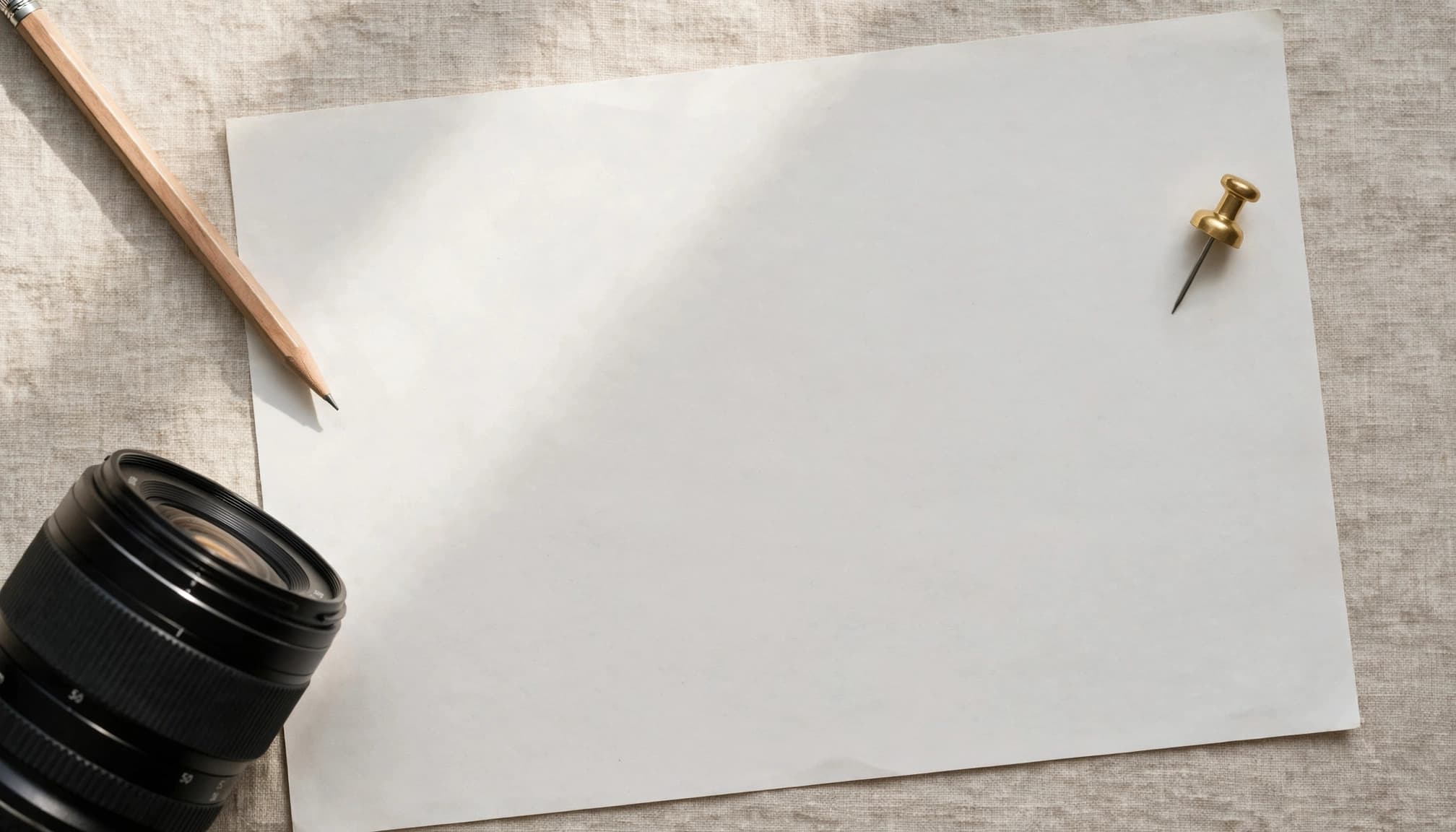 Blank paper, a pencil, camera lens, and map pin token on a table.